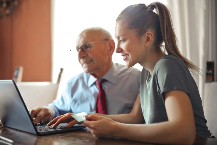 Pensionato al pc con donna giovane - Fonte Pexels