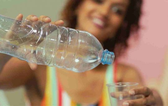 Donna versa acqua in un bicchiere da una bottiglia di plastica